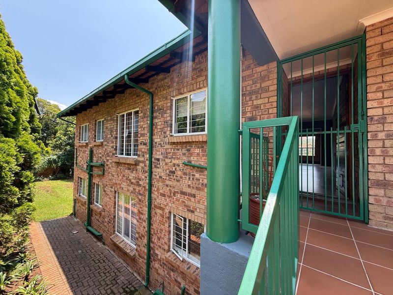 Rear exterior view of the apartment building featuring a brick facade, tiled patio area, and secure metal gate access.