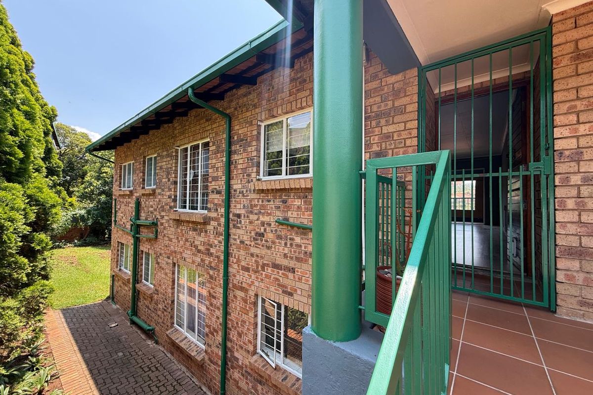 Rear exterior view of the apartment building featuring a brick facade, tiled patio area, and secure metal gate access.