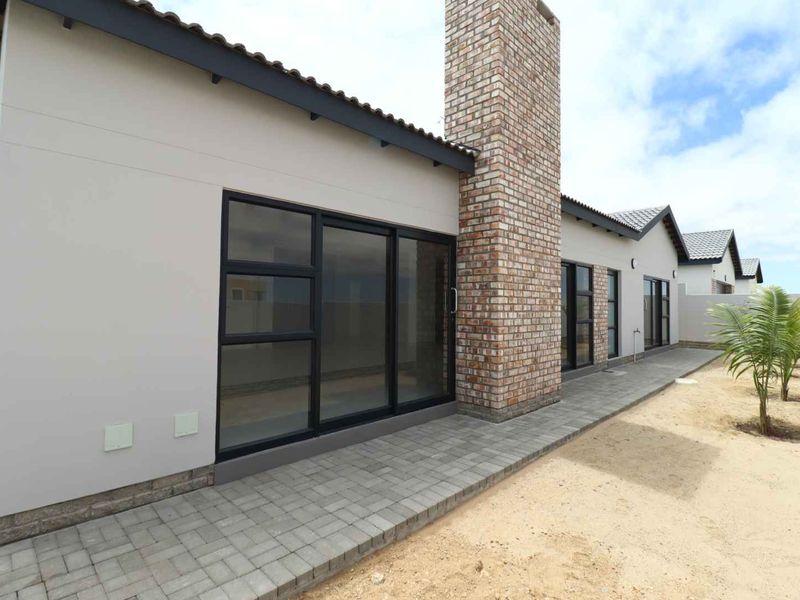 Rear view of the house featuring a brick chimney, paved patio area, and modern black aluminium sliding doors leading into the living space.