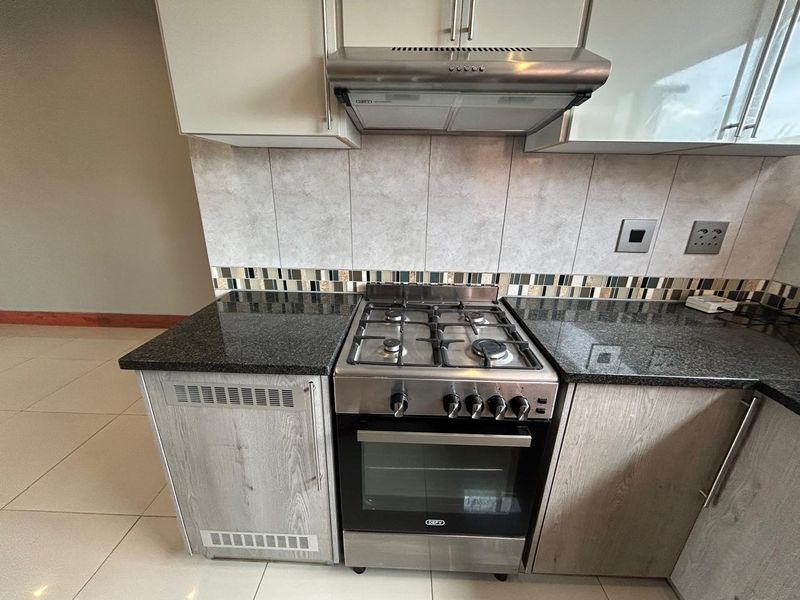 Modern kitchen area featuring granite countertops, a stainless steel gas hob with oven, and a matching extractor fan with tiled backsplash.