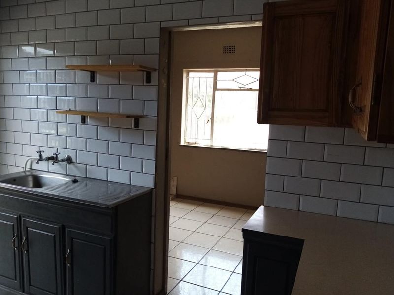 Kitchen area featuring a subway tile backsplash, stainless steel sink, and built-in cabinetry, leading into an adjacent room with tiled flooring.