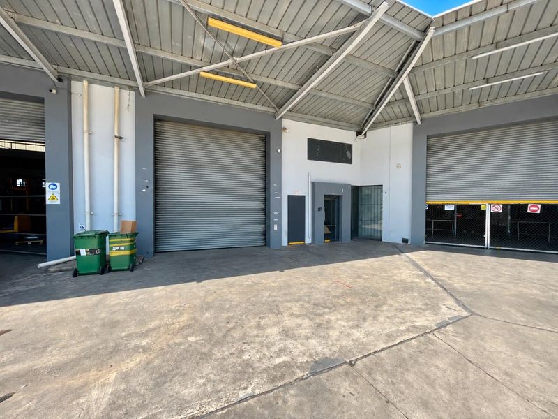 Industrial loading area featuring multiple roller shutter doors, concrete hardstand, and a covered metal roof structure suitable for logistics or storage operations.