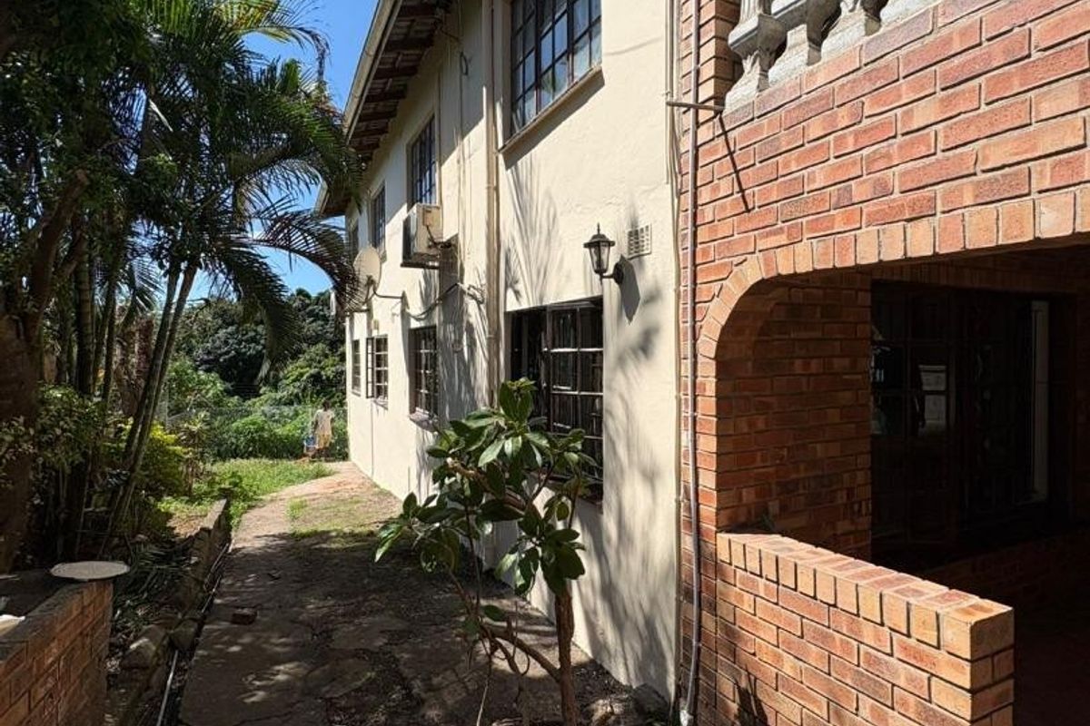 Rear exterior view of the house featuring a brick facade, a covered patio area with a balustrade, and a concrete pathway leading to the garden.