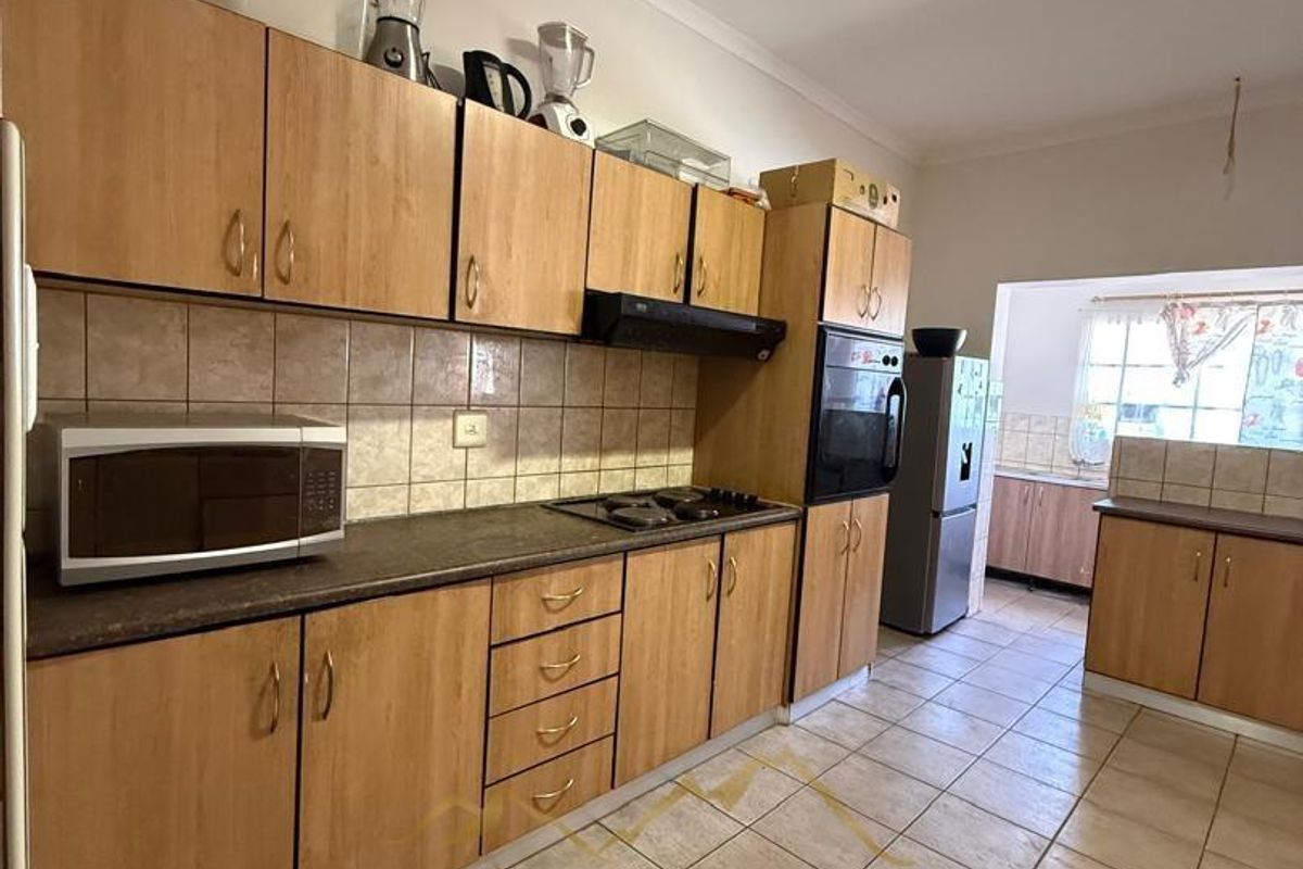 A functional kitchen featuring wood-look cabinetry, tiled splashbacks, built-in oven, and hob, with tiled flooring throughout.