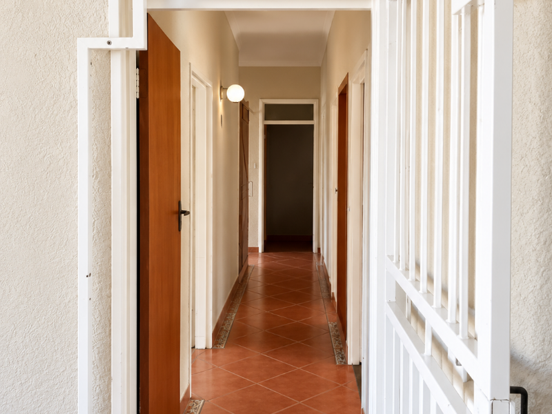 A bright hallway featuring terracotta-style floor tiles with decorative borders, white walls, and a white metal security gate at the entrance.