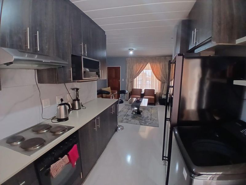 Open-plan kitchen and living area featuring dark wood cabinetry, integrated appliances, tiled flooring, and a bright, connected layout.