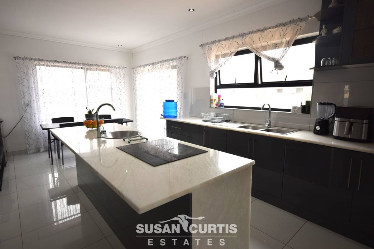 Modern open-plan kitchen featuring a central island with a built-in induction hob, stone countertops, dark cabinetry, and double stainless steel sinks.