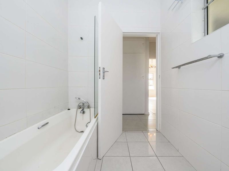 A clean, minimalist bathroom featuring a white bathtub with a glass screen, tiled walls, and neutral floor tiles.