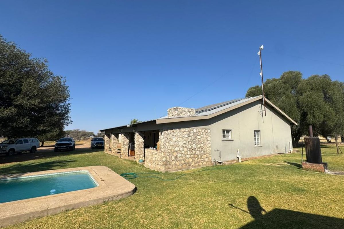 Rear view of a farm property featuring a swimming pool, stone-clad exterior walls, a covered patio area, and solar panels on the roof.