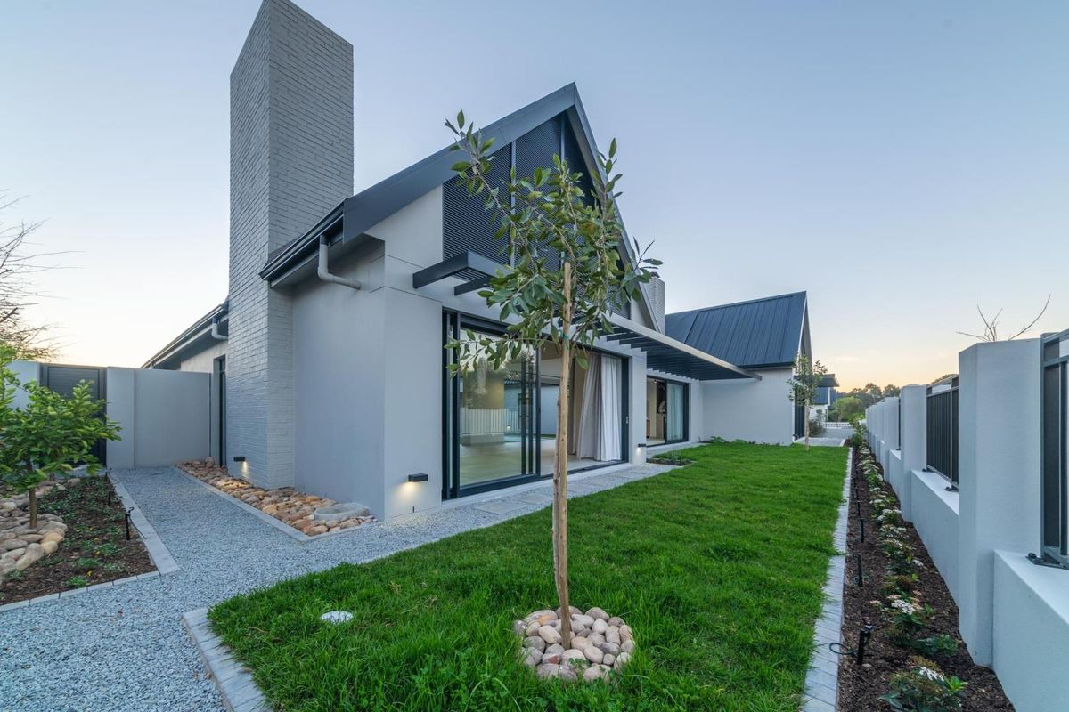 Modern rear elevation featuring a brick chimney, large sliding glass doors, metal roofing, and a well-maintained landscaped garden with gravel pathways.