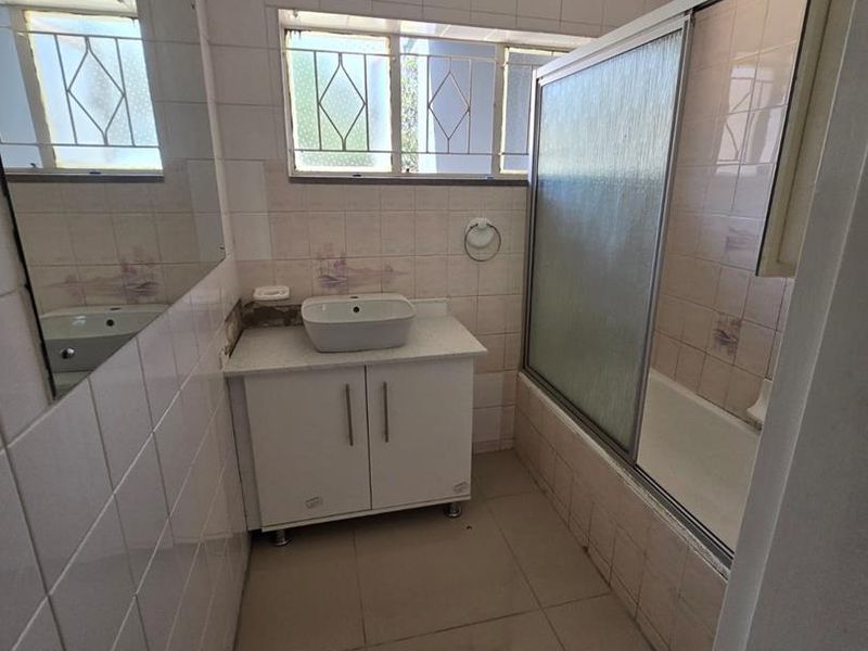 A functional bathroom featuring a vanity with a vessel sink, a bathtub with a sliding shower screen, and tiled finishes throughout.