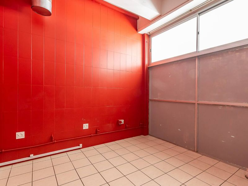 An empty utility space featuring bright red tiled walls, tiled flooring, exposed electrical conduit, and high-level windows providing natural light.