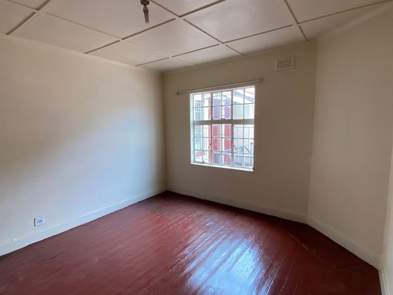 A vacant bedroom featuring original timber flooring, a tiled ceiling, and a single window providing natural light.