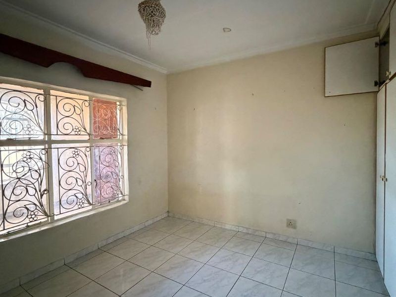 An empty bedroom featuring tiled flooring, built-in cupboards, and security bars on the window, offering a blank canvas for potential updates.