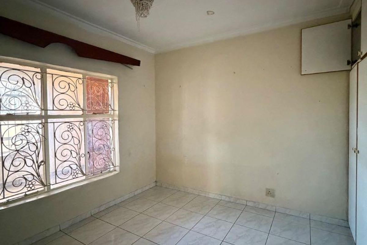 An empty bedroom featuring tiled flooring, built-in cupboards, and security bars on the window, offering a blank canvas for potential updates.