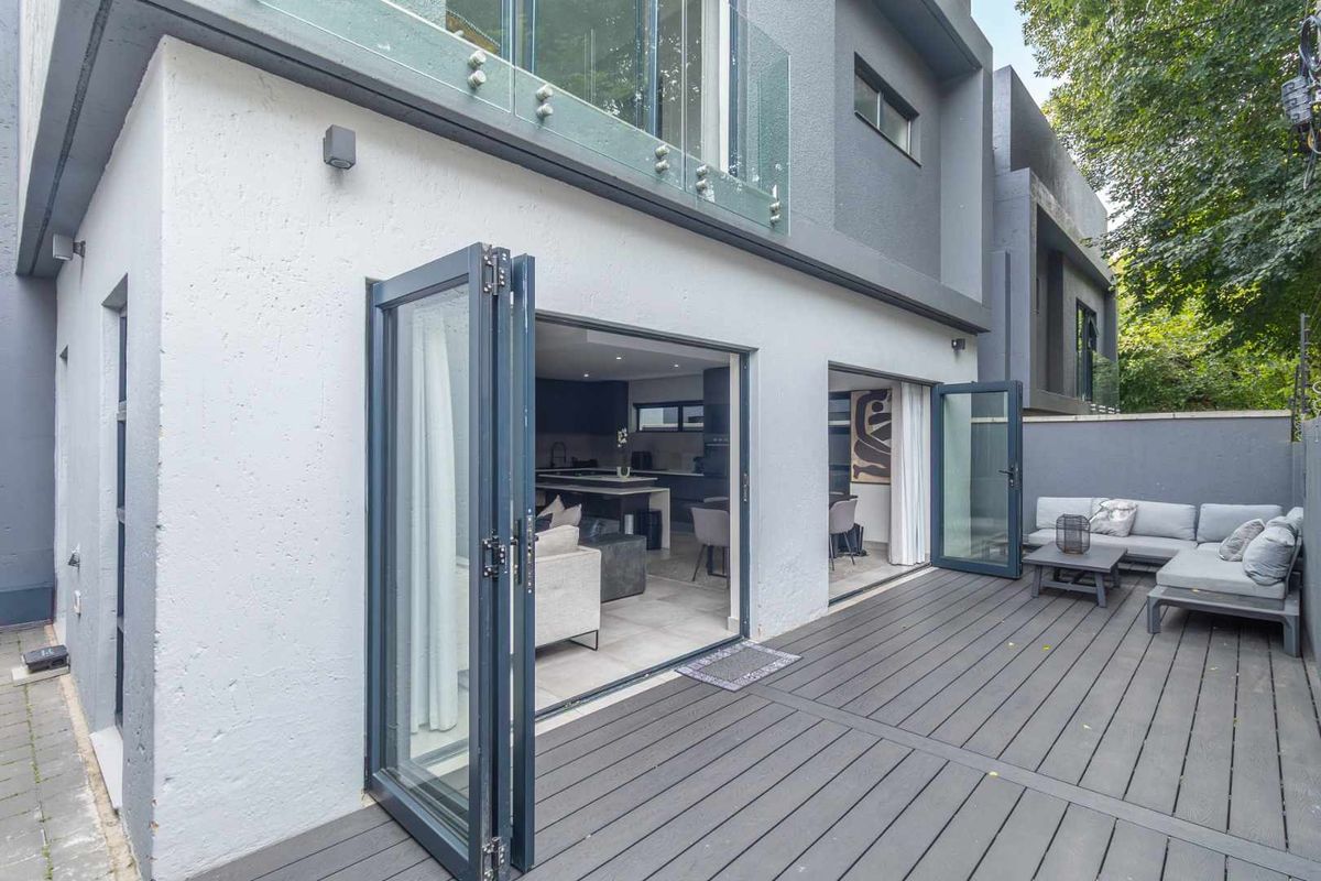 Modern townhouse rear exterior featuring a composite deck patio with seamless indoor-outdoor flow through large folding glass doors to the open-plan living area.