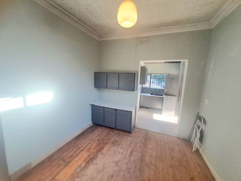 Open plan living area featuring original timber flooring and decorative pressed metal ceilings, leading through to a separate kitchen space.