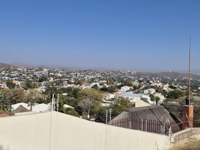 An elevated view overlooking the surrounding residential neighborhood and distant hills, featuring a perimeter wall with electric fencing in the foreground.