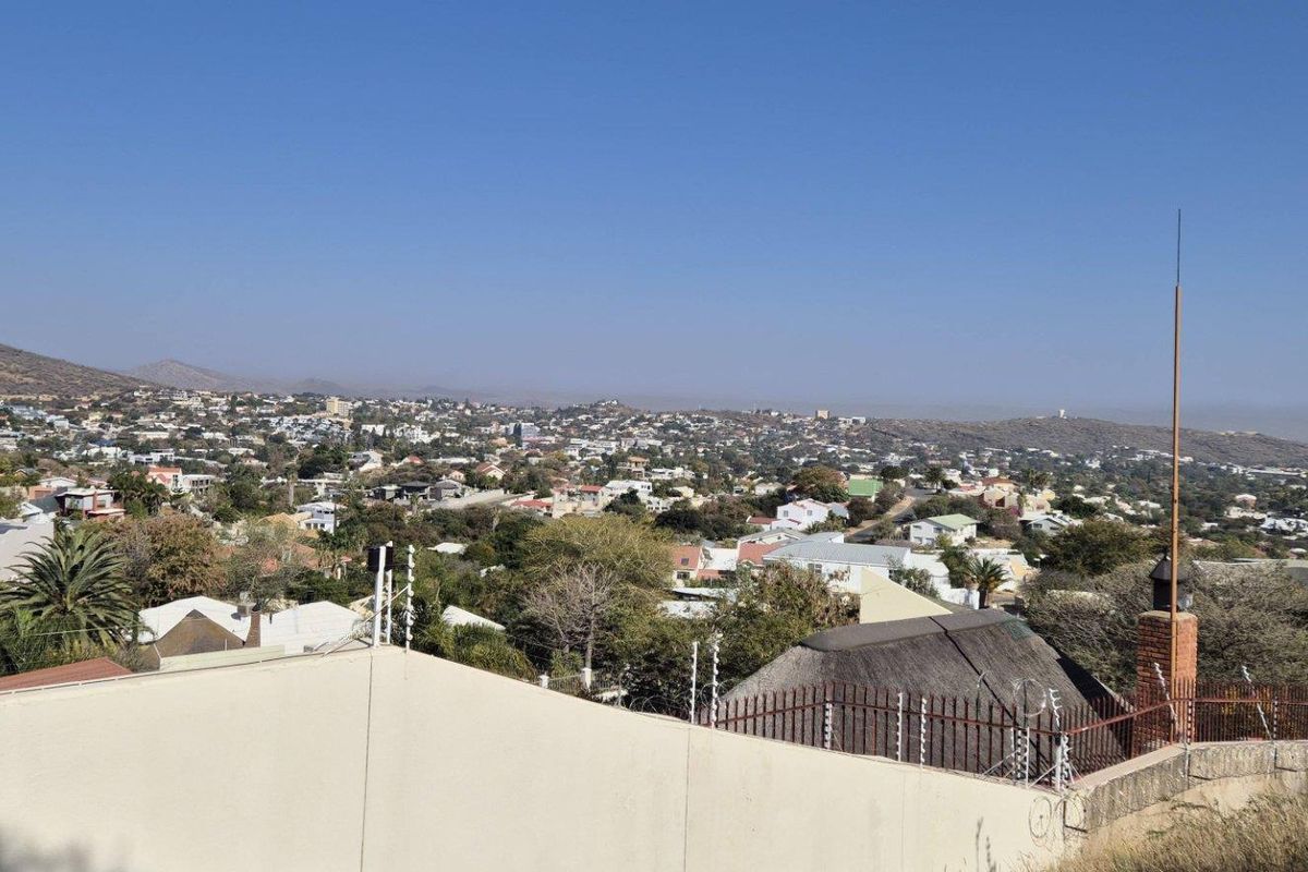 An elevated view overlooking the surrounding residential neighborhood and distant hills, featuring a perimeter wall with electric fencing in the foreground.