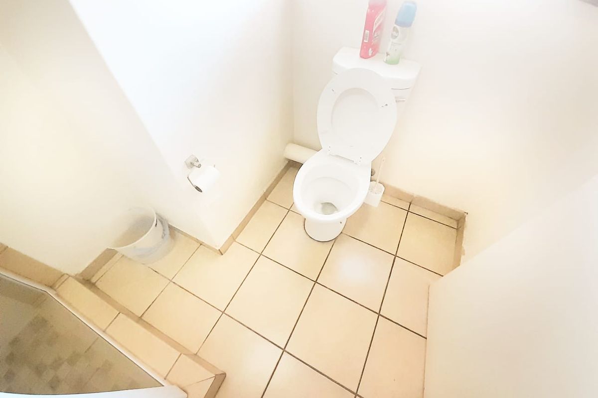 A functional bathroom featuring a standard toilet, tiled flooring, and a shower enclosure.