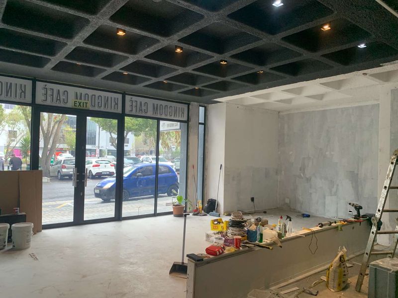 Open-plan retail space currently under renovation, featuring a distinctive waffle slab ceiling, large glass storefront, and a built-in service counter.