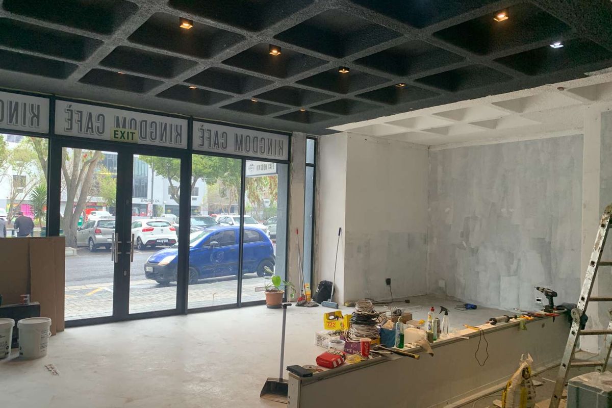 Open-plan retail space currently under renovation, featuring a distinctive waffle slab ceiling, large glass storefront, and a built-in service counter.