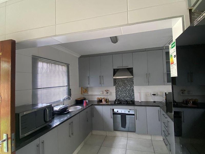 Modern kitchen featuring grey cabinetry, granite countertops, built-in oven, gas hob, extractor fan, and tiled flooring.