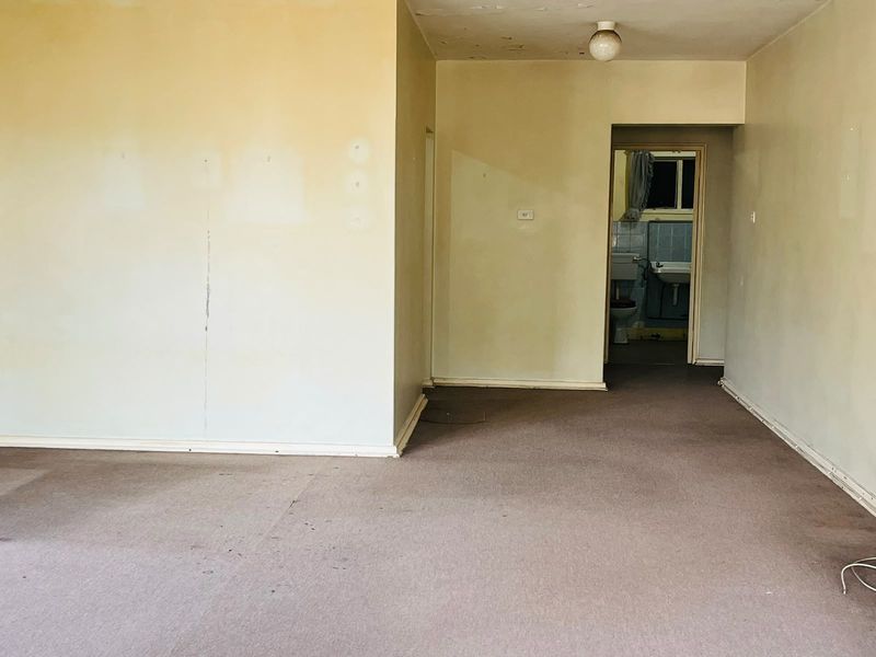 An empty living area featuring carpet flooring and neutral walls, requiring cosmetic updates and refurbishment to restore its appeal.