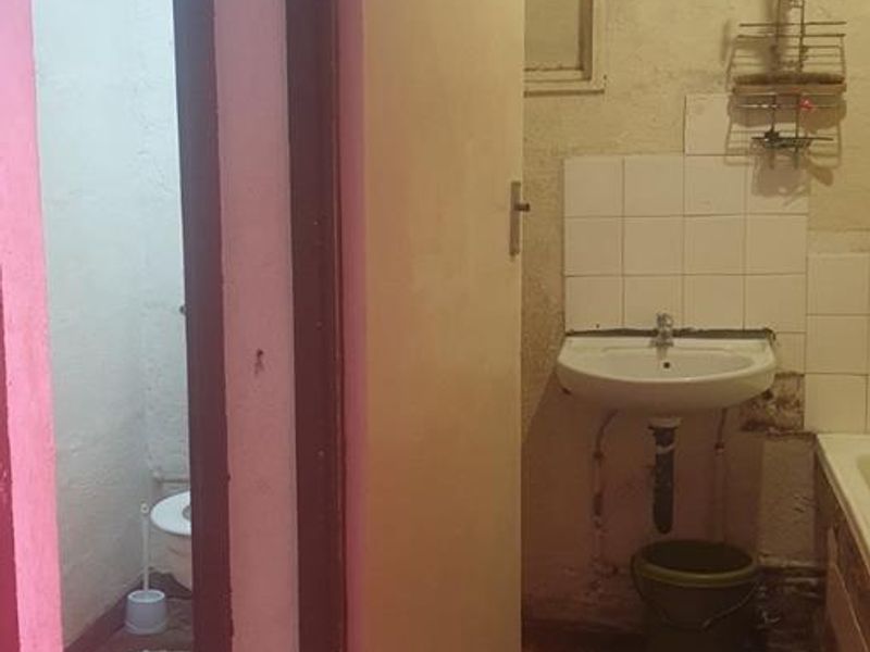 A dated bathroom and separate toilet area requiring significant renovation, featuring basic sanitary fixtures and worn wall and floor finishes.