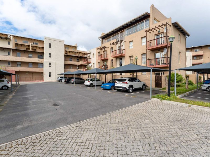 Exterior view of a multi-story apartment complex featuring paved parking areas with shade cloth carports and building balconies.