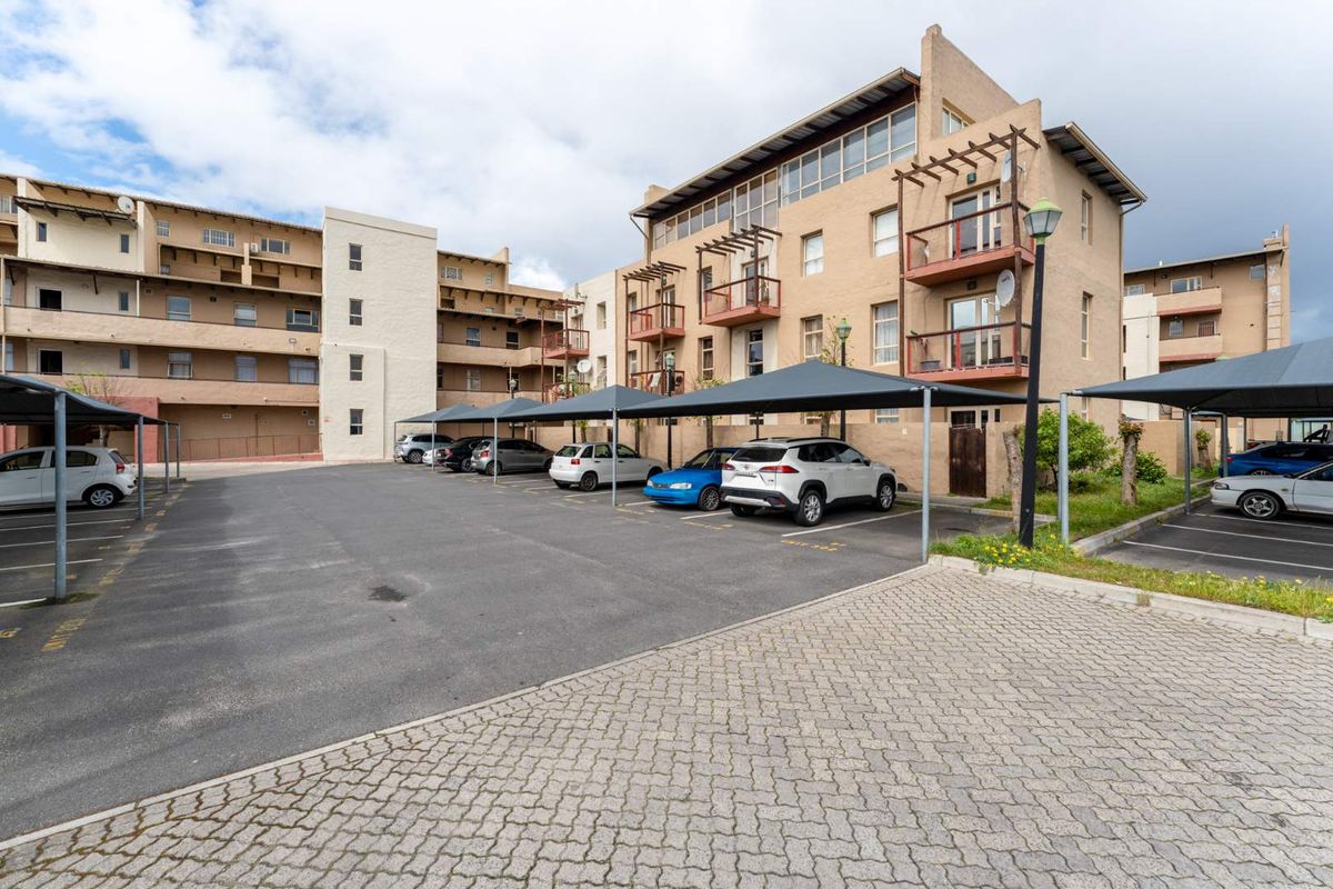 Exterior view of a multi-story apartment complex featuring paved parking areas with shade cloth carports and building balconies.