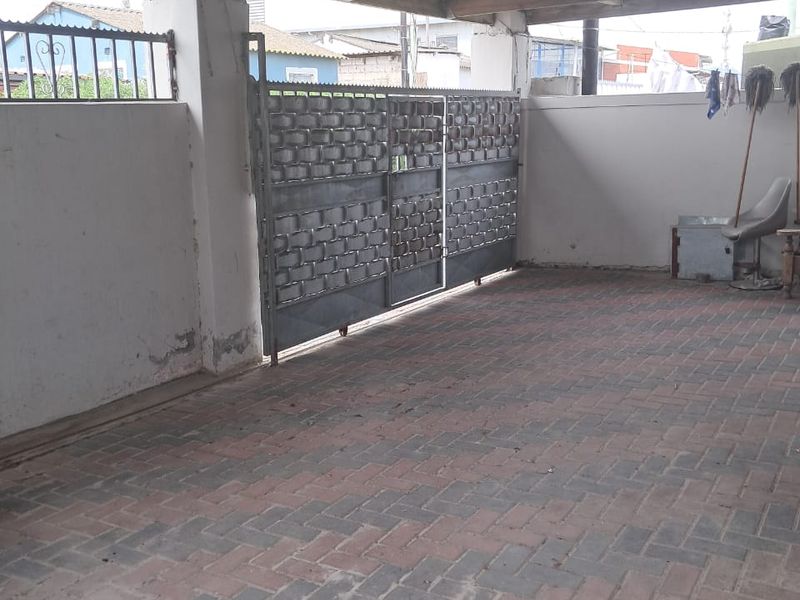 A covered outdoor parking area featuring a paved floor, metal sliding gate, and perimeter walling with security fencing.