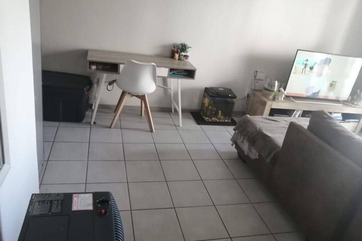 A living room area featuring neutral ceramic floor tiles and a functional layout suitable for a combined lounge and workspace.