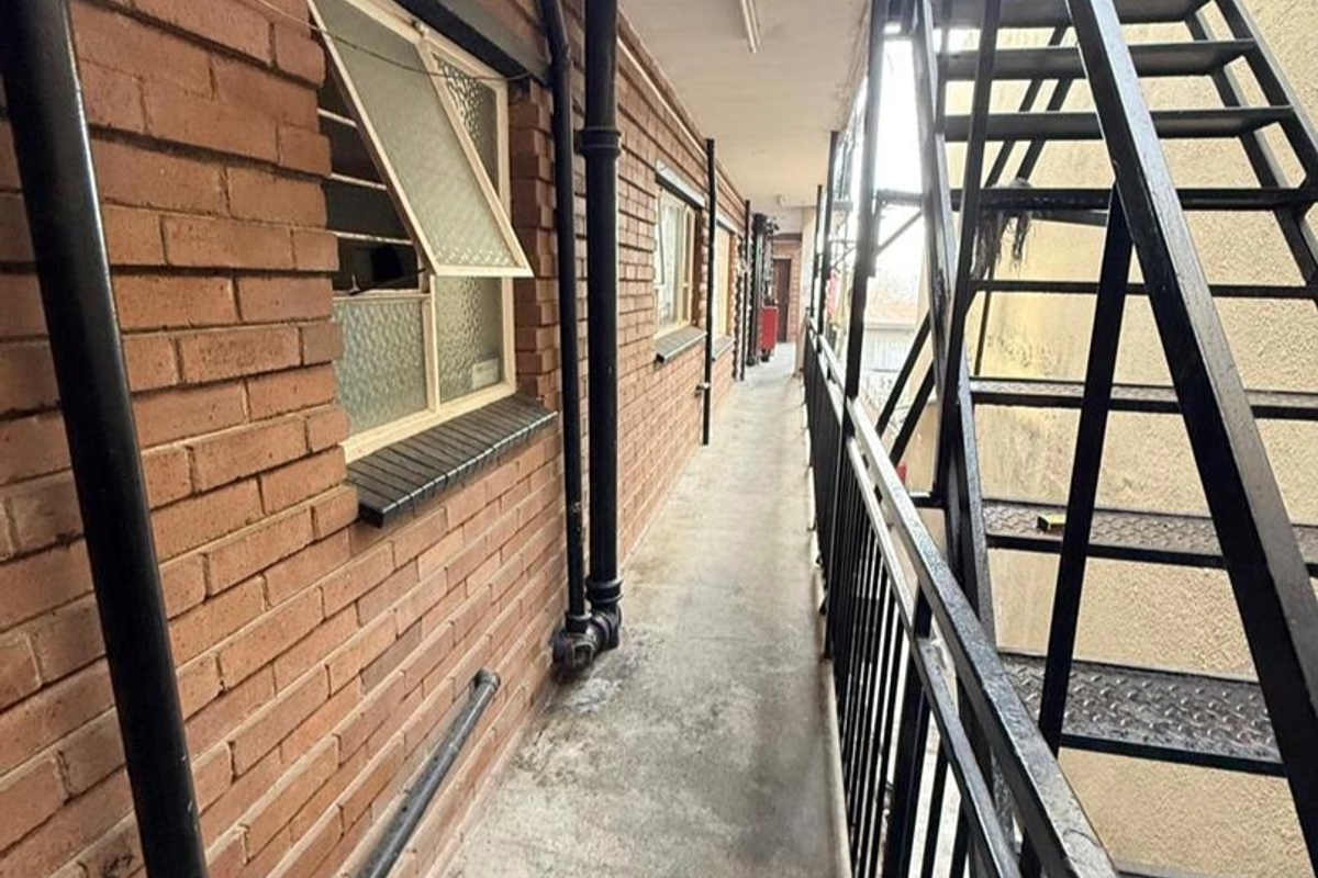Exterior walkway featuring exposed brick walls, metal staircase access, and concrete flooring in an apartment complex setting.