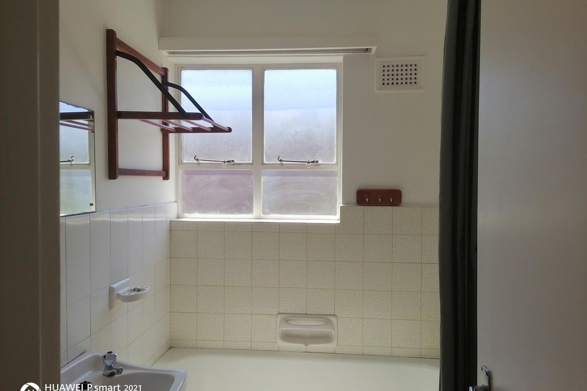 A functional bathroom featuring a bathtub, wall-mounted basin, and tiled splashback, offering a blank canvas for modern renovation and aesthetic updates.