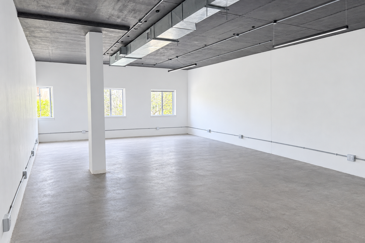 A spacious, modern open-plan office featuring polished concrete floors, an exposed industrial ceiling with HVAC ducting, and clean white walls.