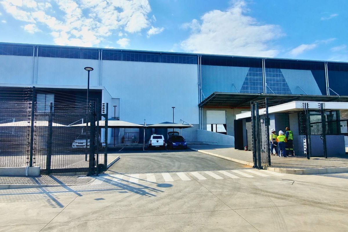 Front view of an industrial facility featuring a secure gated entrance, guard house, covered parking bays, and large-scale metal cladding exterior.