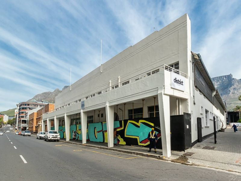 Street-level view of a commercial building featuring a covered walkway, balcony, and prominent signage, situated in an urban setting.
