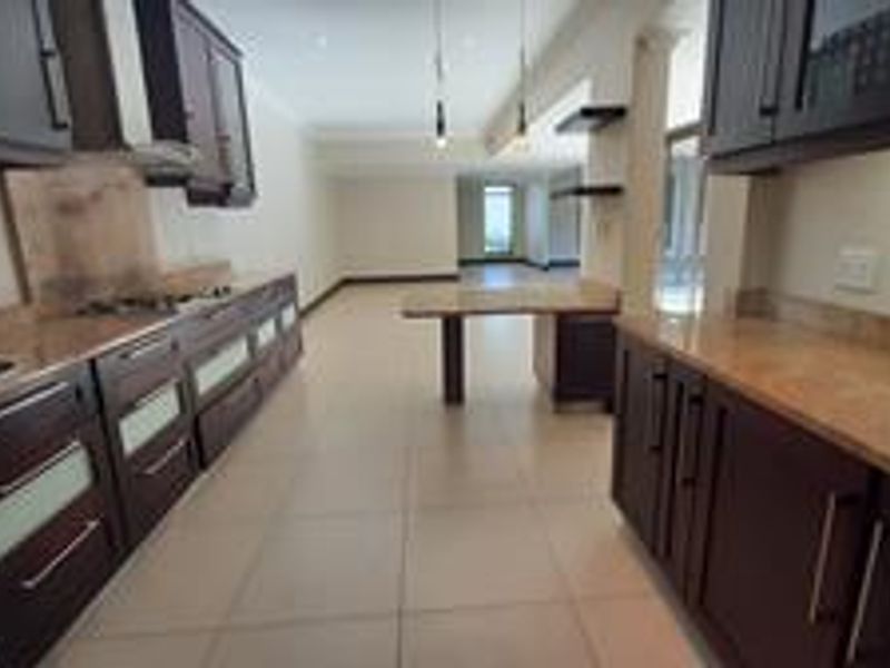 Spacious kitchen featuring dark wood cabinetry, stone countertops, a gas hob, and a built-in breakfast bar, leading into an open-plan living area.