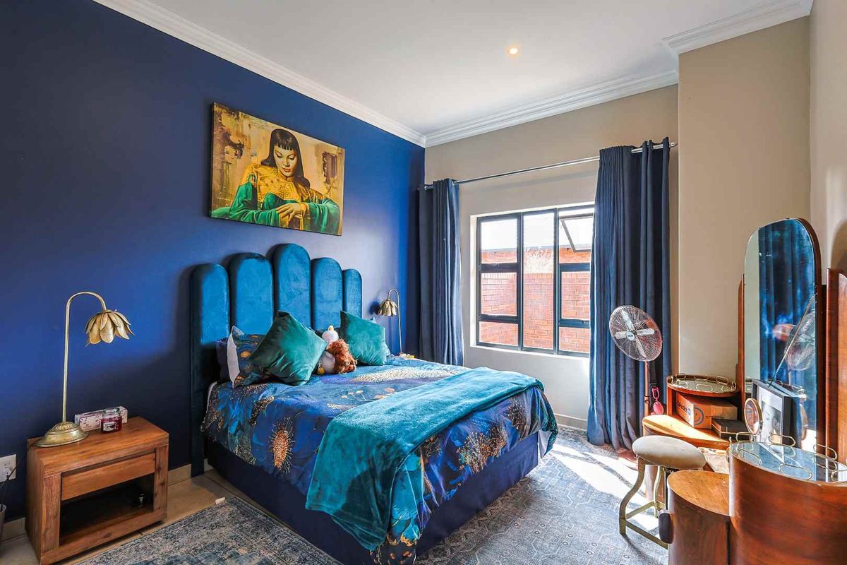 A well-maintained bedroom featuring a bold blue accent wall, recessed downlighting, and a large window providing natural light.
