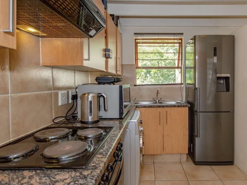 Functional kitchen featuring wood-finish cabinetry, granite-look laminate countertops, electric hob with extractor, and tiled backsplash, offering a practical layout for daily use.