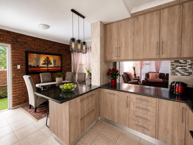 Open-plan kitchen and dining area featuring modern laminate cabinetry, granite countertops, and a striking exposed brick feature wall.