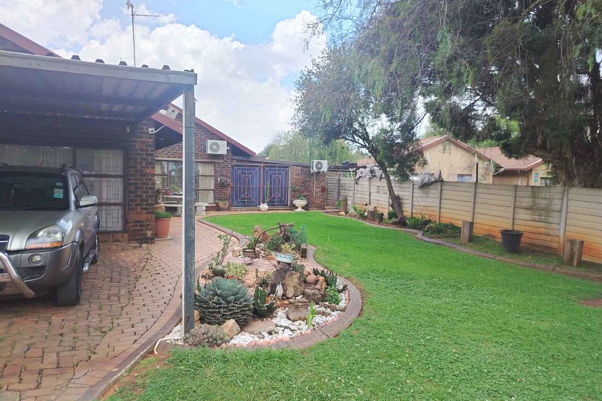 A spacious rear garden featuring a manicured lawn, landscaped rockery, and a covered carport area adjacent to the main dwelling.