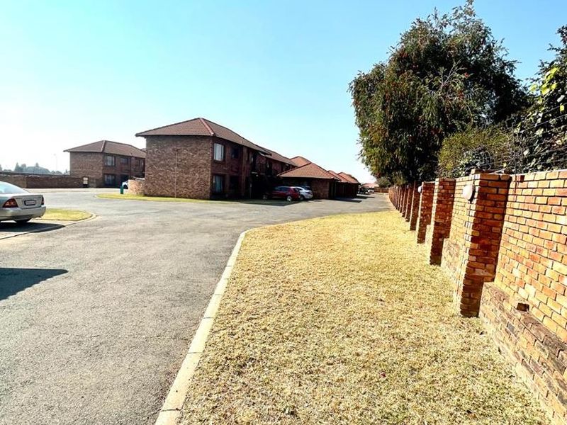 View of the complex exterior featuring facebrick buildings, paved driveway, and a brick boundary wall.