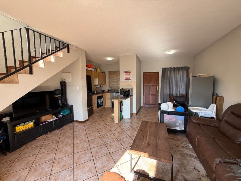 Open-plan living area featuring tiled flooring, a staircase with wrought iron balustrade, and a functional kitchen with built-in cabinetry and appliances.