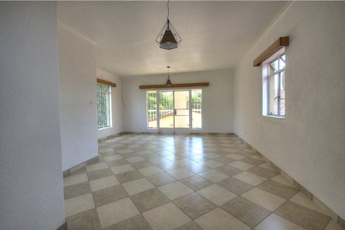 A spacious, empty living area featuring neutral tiled flooring, large windows with security bars, and sliding glass doors leading to the exterior.