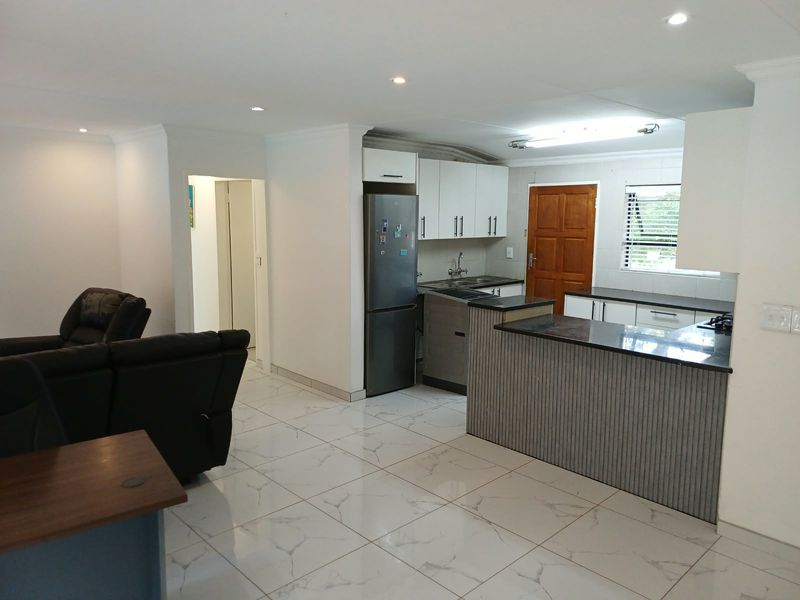 Open plan kitchen and living area featuring modern tiled flooring, built-in cabinetry with granite countertops, and a functional breakfast bar layout.
