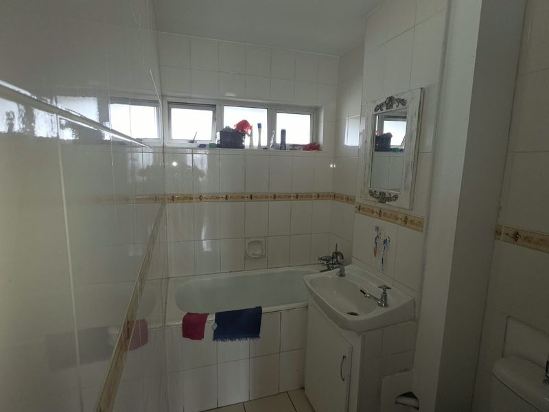 A functional bathroom featuring a built-in bathtub, vanity basin, and full-height wall tiling, offering a classic layout with potential for modern updates.