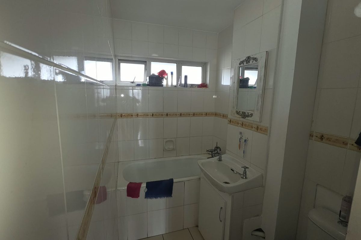 A functional bathroom featuring a built-in bathtub, vanity basin, and full-height wall tiling, offering a classic layout with potential for modern updates.