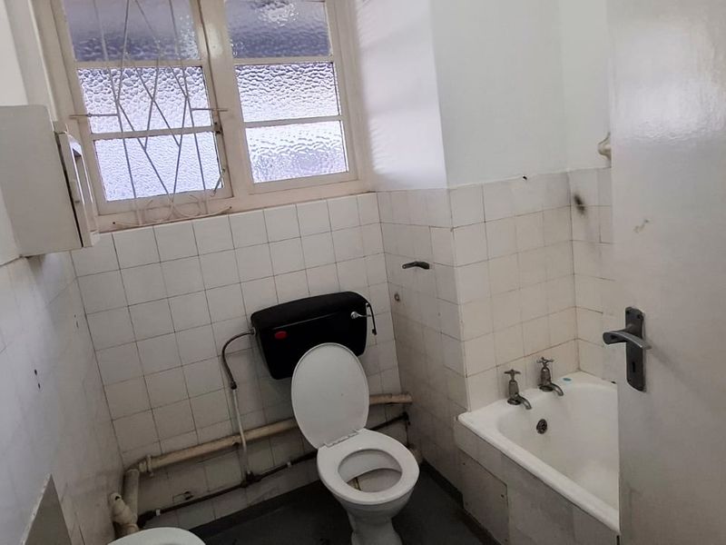 A dated bathroom featuring a bathtub, toilet, and tiled walls, requiring renovation to update the fixtures and finishes.